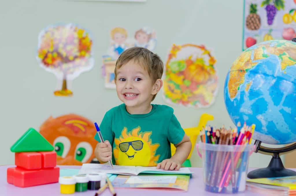 Fröhliches Kind beim Malen an Tisch mit Farben und Globus