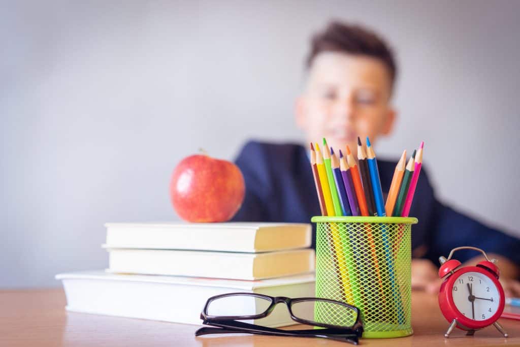 Stifteköcher, Brille, Bücher, Apfel und Wecker vor einem Schuljungen