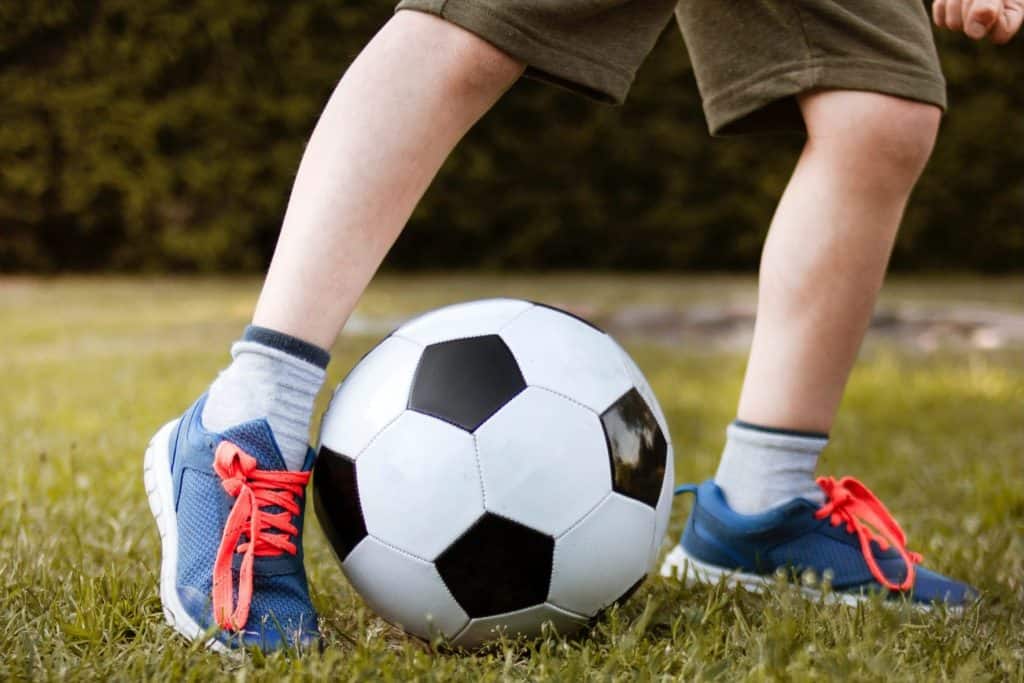 Kinderbeine mit Fußball auf Rasen