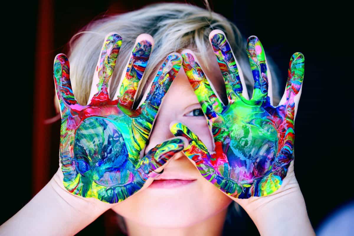 Kind hält bunt bemalte Hände vors Gesicht. Quelle: pexels.com