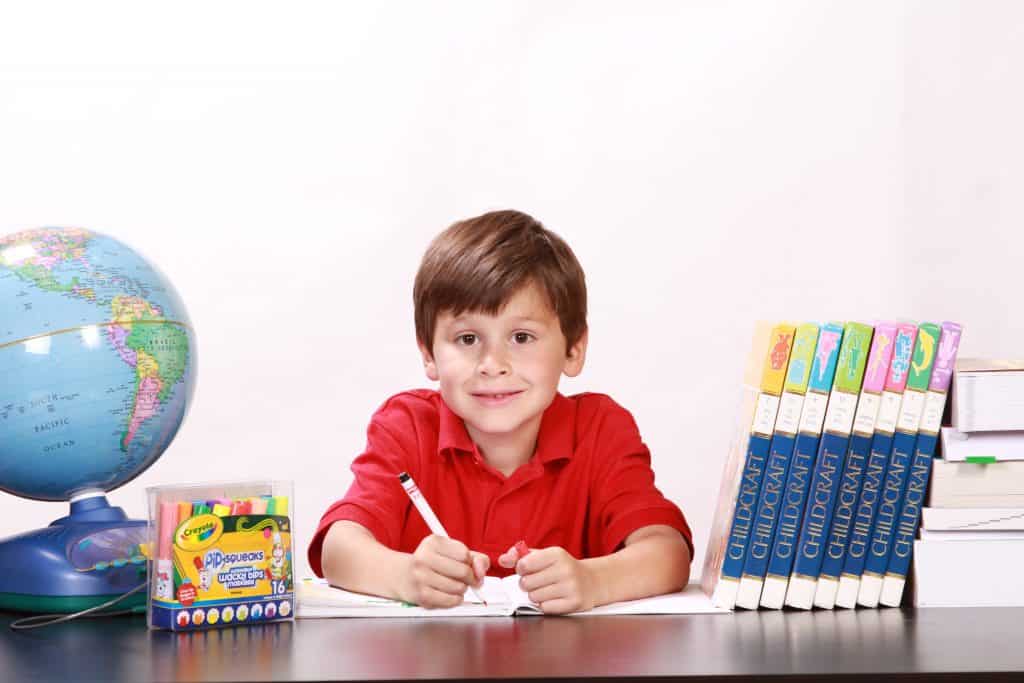 Kind beim Schreiben an Tisch mit Büchern, Farben und Globus
