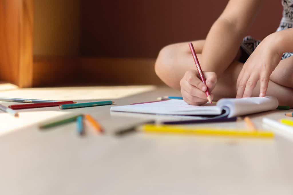 Kind schreibt mit Buntstiften in ein Heft
